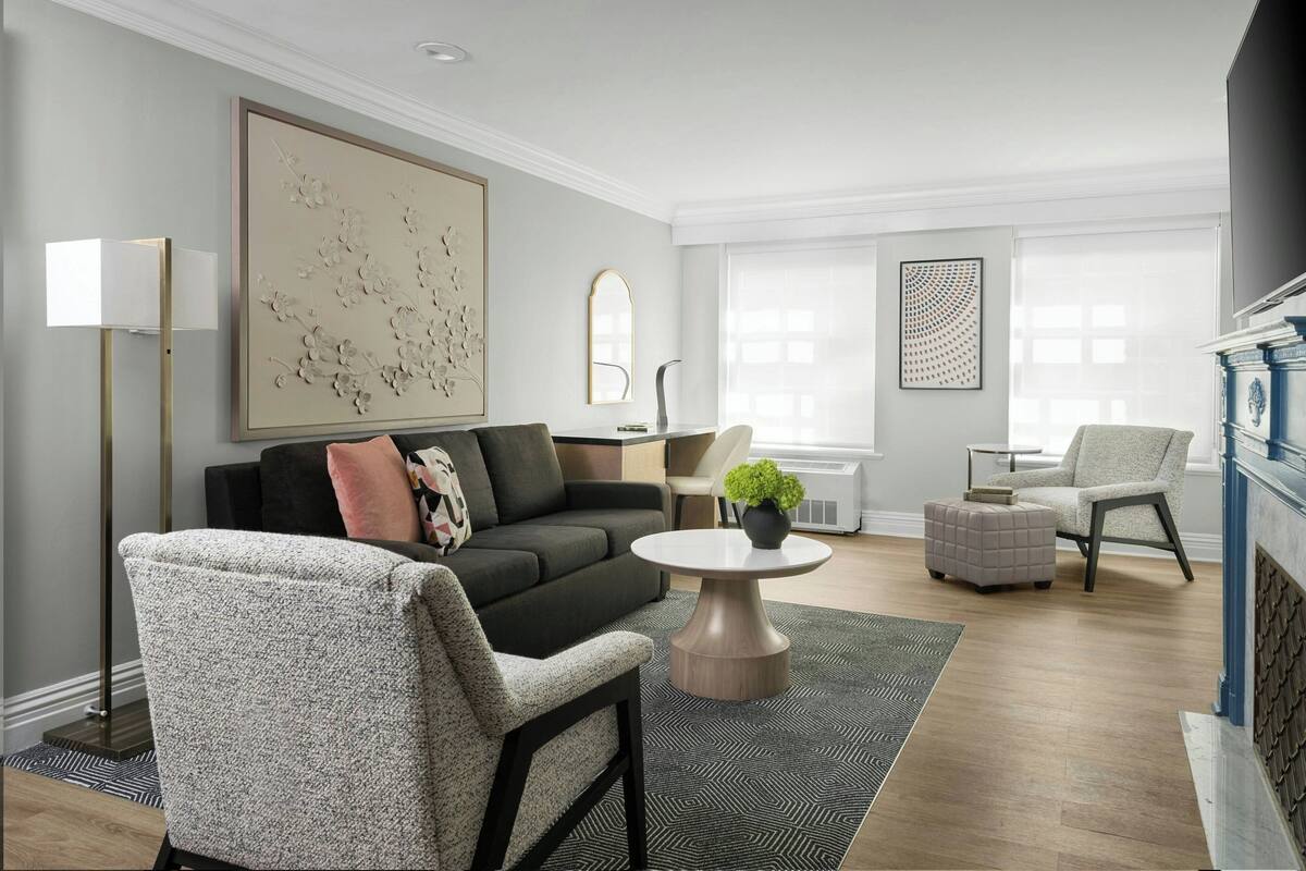 Ein modernes Wohnzimmer mit einem dunkelgrauen Sofa, einem hellen Sessel, einem runden Couchtisch und einem großen abstrakten Gemälde an der Wand.
