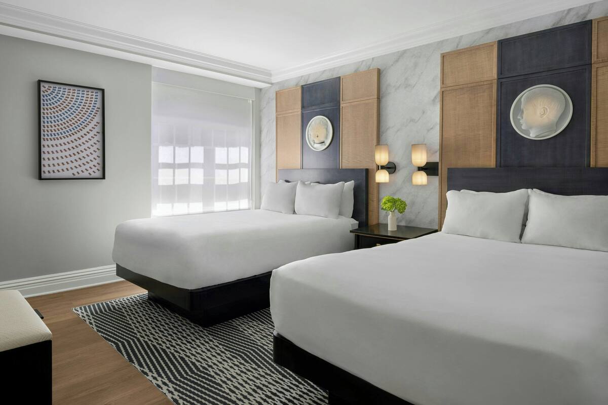 Ein Hotelzimmer mit zwei Betten, einem großen Fenster, einer Marmorwand und einer modernen Leuchte.