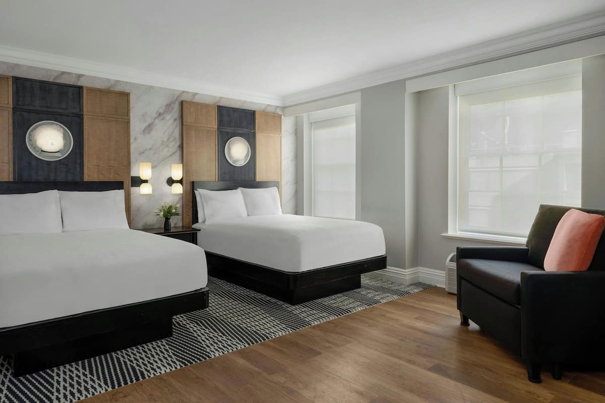 Ein Hotelzimmer mit zwei Betten, einem Sofa und einem großen Fenster.
