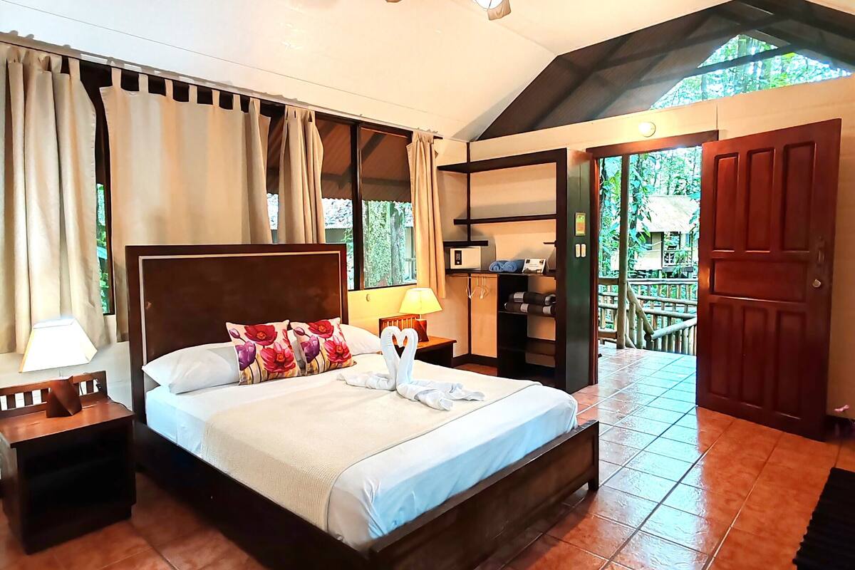 A hotel room with a bed, a nightstand, a ceiling fan, and a view of the outside.