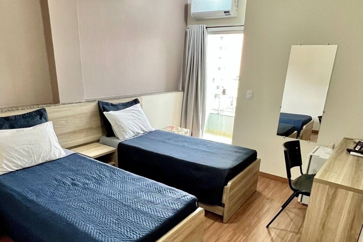 A hotel room with two beds, a desk, a chair, and a mirror.