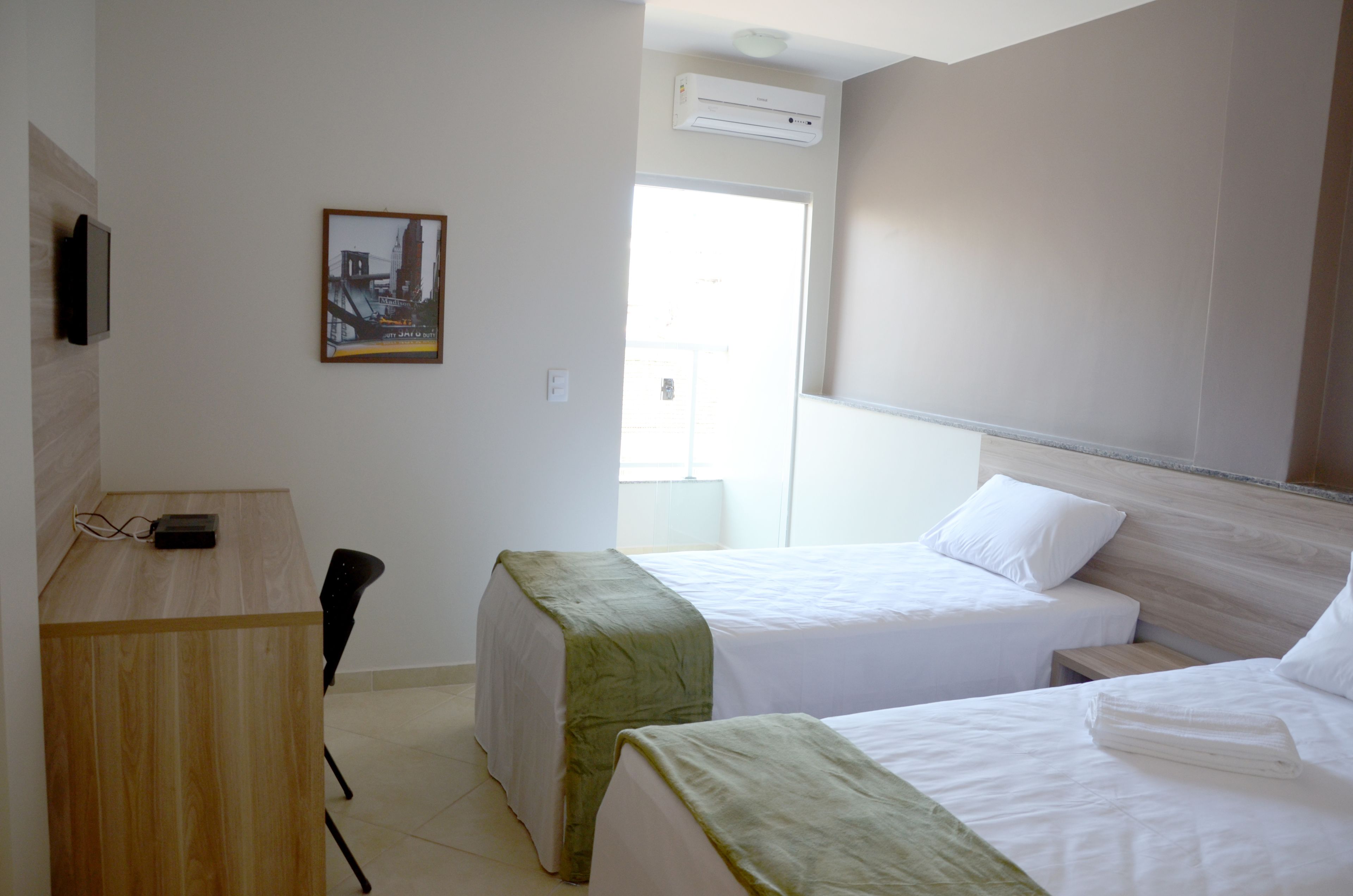 Ein Hotelzimmer mit zwei Betten, einem Schreibtisch, einem Sessel und einer Klimaanlage.