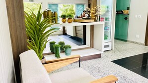 Un vestíbulo de hotel moderno con área de descanso, plantas en macetas, mostrador de recepción y puerta de vidrio que da al área de recepción.