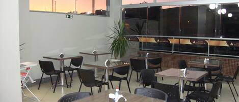 A restaurant with multiple tables and chairs, a large window with a view, and a potted plant.