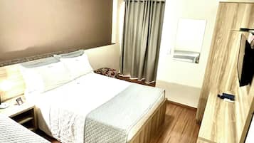 Una habitación de hotel con cama, escritorio, silla, televisor y un mueble pequeño.