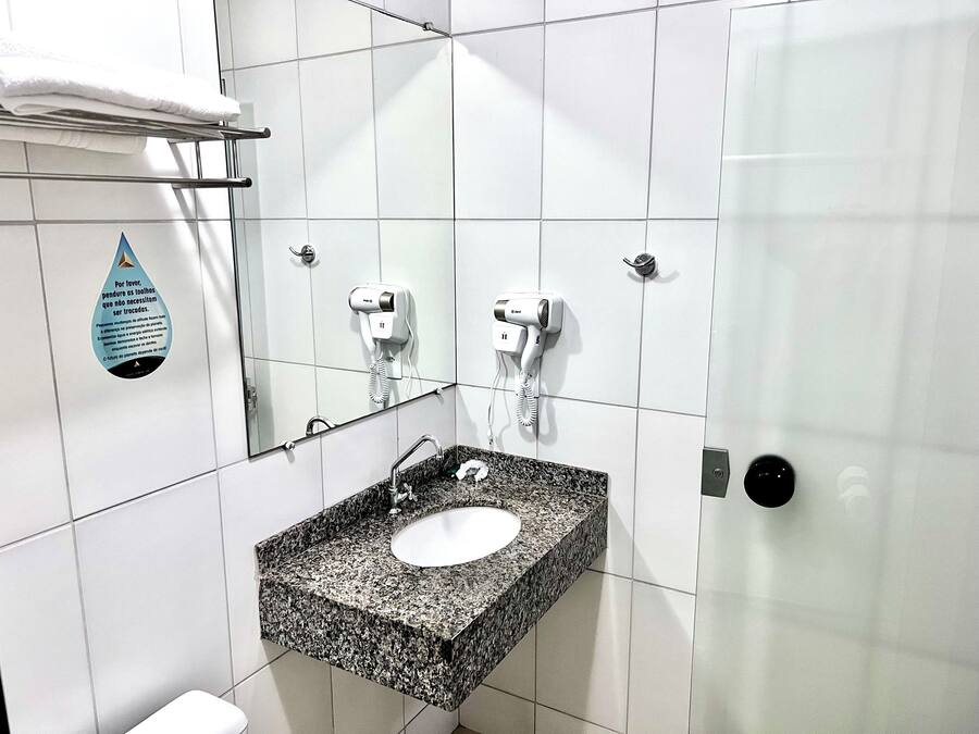 A bathroom with a granite sink, two hair dryers mounted on the wall, and a towel rack with folded towels.