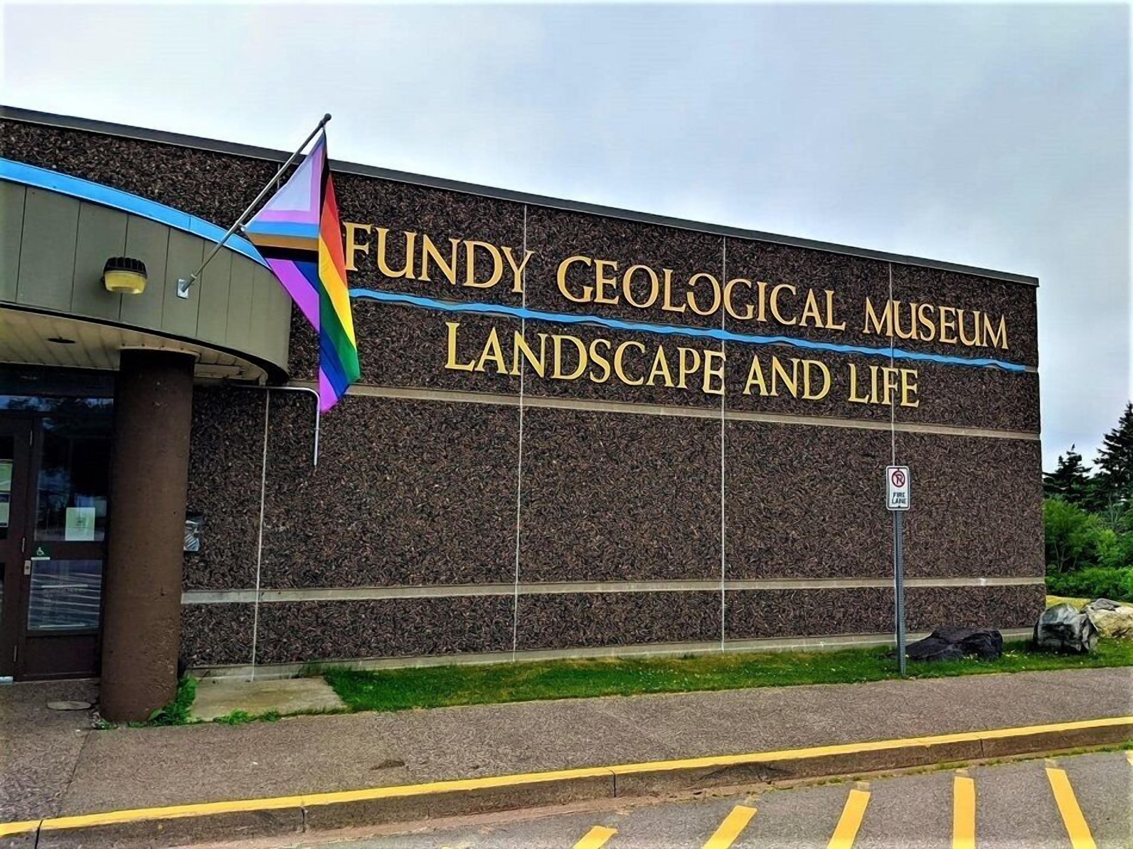 The exterior of the Fundy Geological Museum, featuring a prominent sign with the museum's name and a colorful flag.