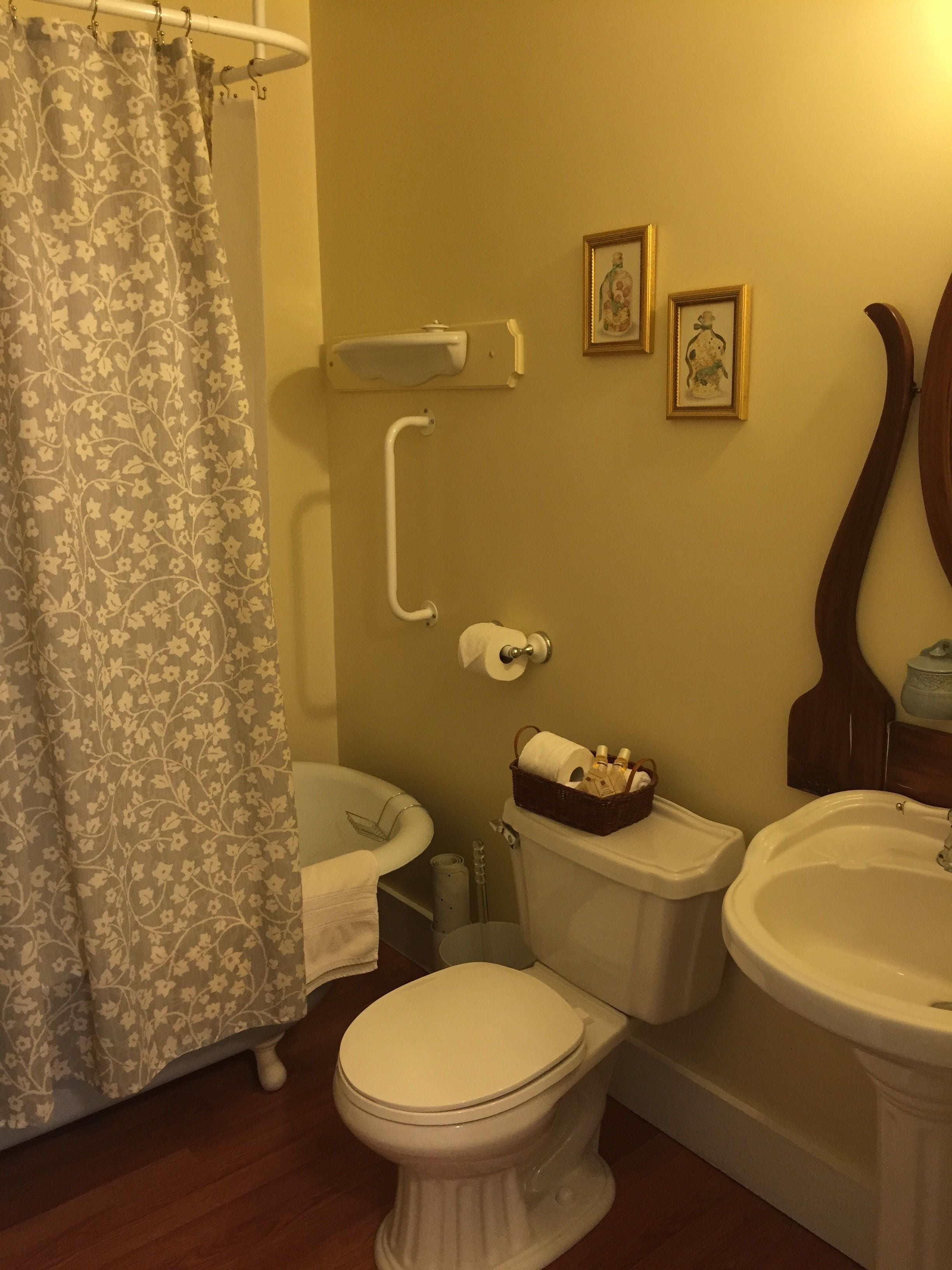Un baño con inodoro, bidé y lavamanos. Hay dos cuadros enmarcados en la pared.