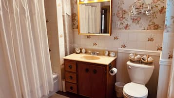 Un baño con tocador de madera, lavamanos, espejo con iluminación, inodoro y cortina de ducha.