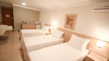 Quarto de hotel com duas camas de solteiro, uma escrivaninha, uma cadeira, uma pequena cozinha e um aparelho de ar condicionado.