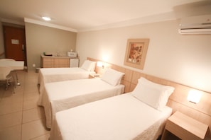 Habitación de hotel con dos camas individuales, un escritorio, una silla, una kitchenette pequeña y un equipo de aire acondicionado.
