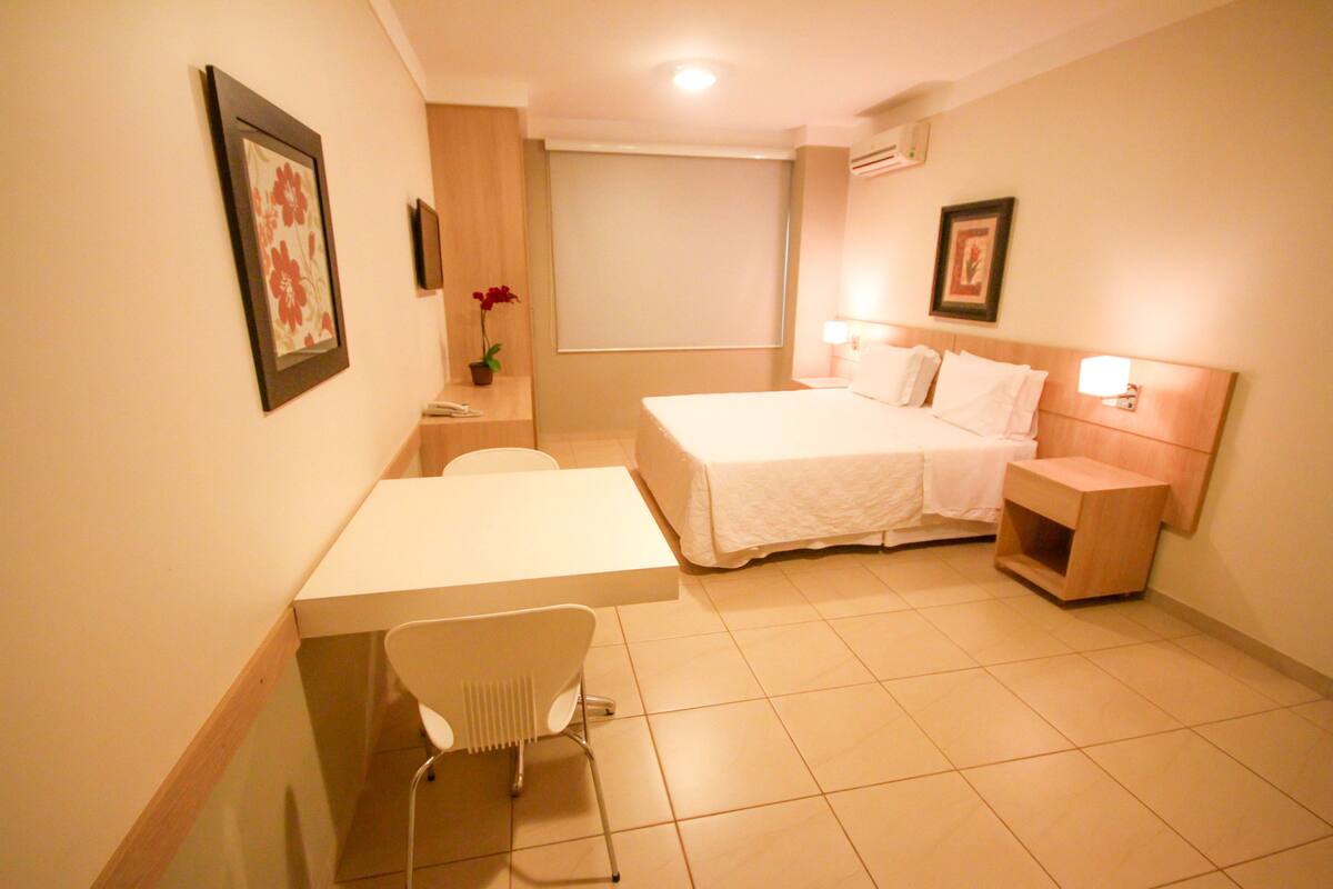 Une chambre d’hôtel avec un lit, une table de chevet, une chaise et un petit bureau.