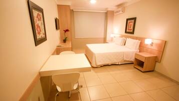 Quarto de hotel com cama, mesa de cabeceira, cadeira e pequena escrivaninha.