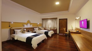 A hotel room with two beds, wooden flooring, a wooden door, a TV, and a desk with a chair.