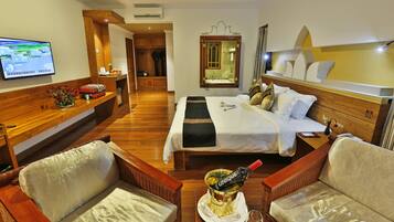 A hotel room with a bed, two armchairs, a TV, a wooden desk, and a bottle of champagne.