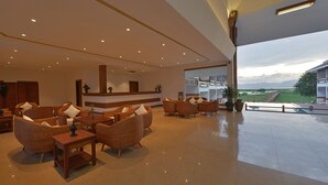Eine geräumige Lobby mit Korbmöbeln, einem Empfangstresen und einem großen Fenster mit Blick auf eine Brücke und die Landschaft.