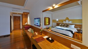 Ein Hotelzimmer mit einem Holztisch, einem Bett mit Kopfteil, einem großen Spiegel, einem Fernseher und einer Holztür.