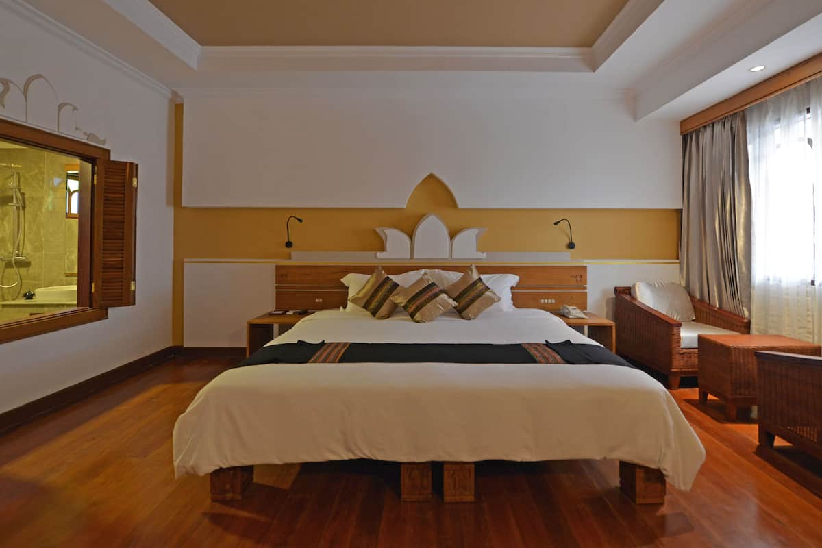 A hotel room with a large bed, a wooden headboard, a nightstand, a chair, and a mirror.