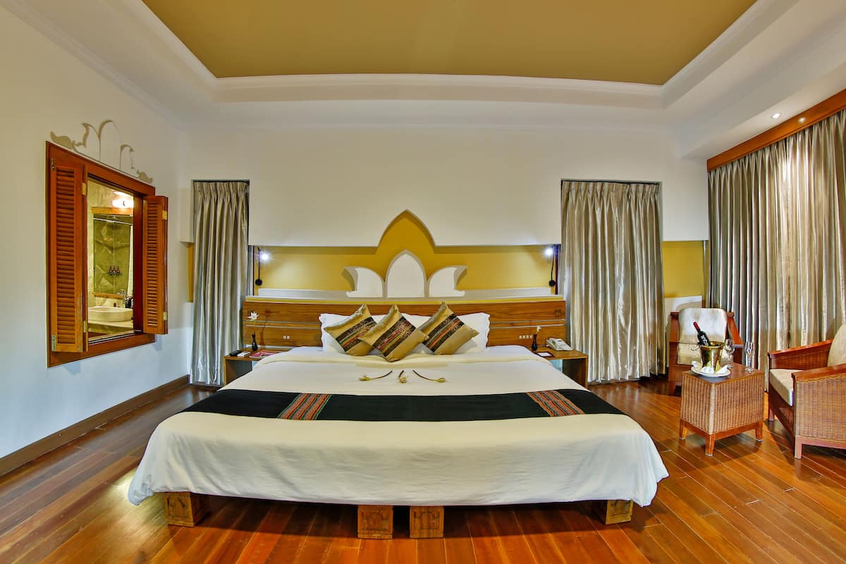 A spacious hotel room with a large bed, wooden floor, and a classic design.