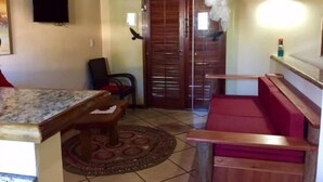 Une pièce avec une table en bois, un banc rembourré de couleur rouge, un tapis à motifs et une porte dotée d’un volet en bois.