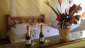 Un lit avec une literie à motifs floraux, une tête de lit en bois et un vase rempli de fleurs rouges posé sur une table.