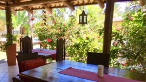 Une terrasse extérieure avec une table et des chaises en bois, entourée d’une végétation luxuriante et de plantes en fleurs.