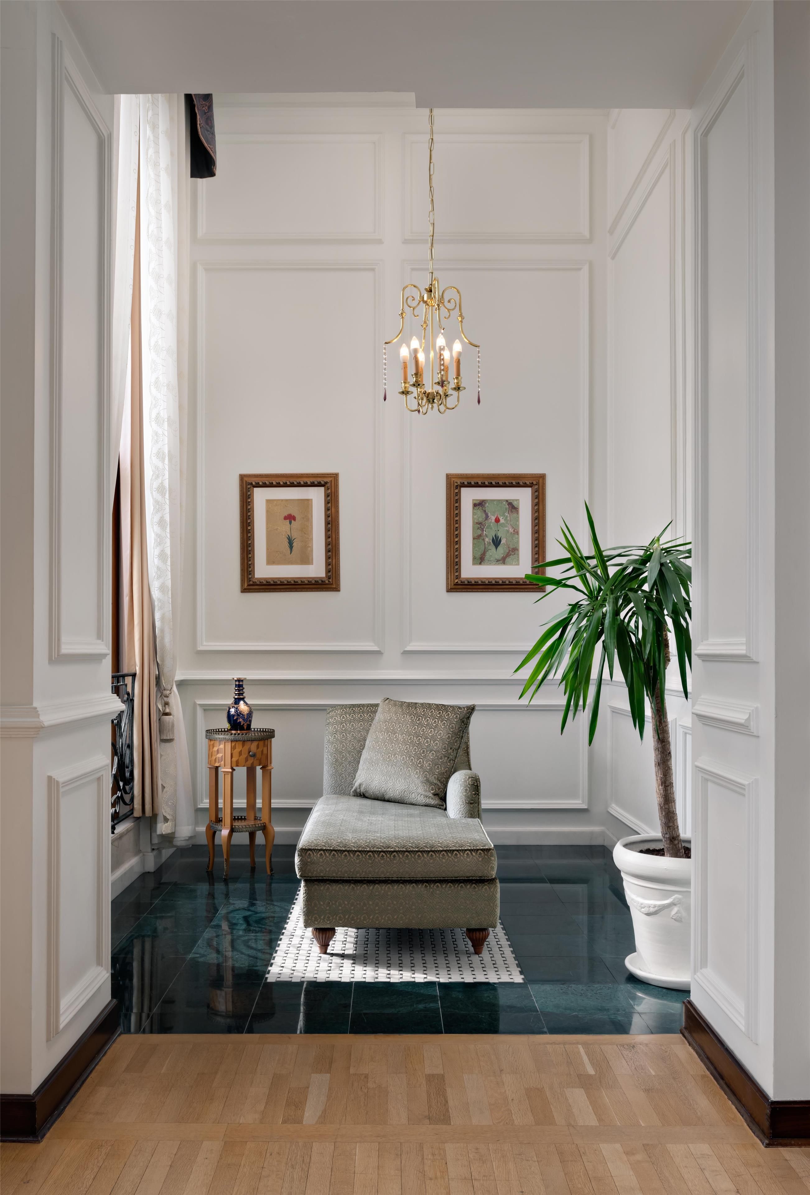A room with a patterned sofa, a chandelier, framed artwork, and a potted plant.