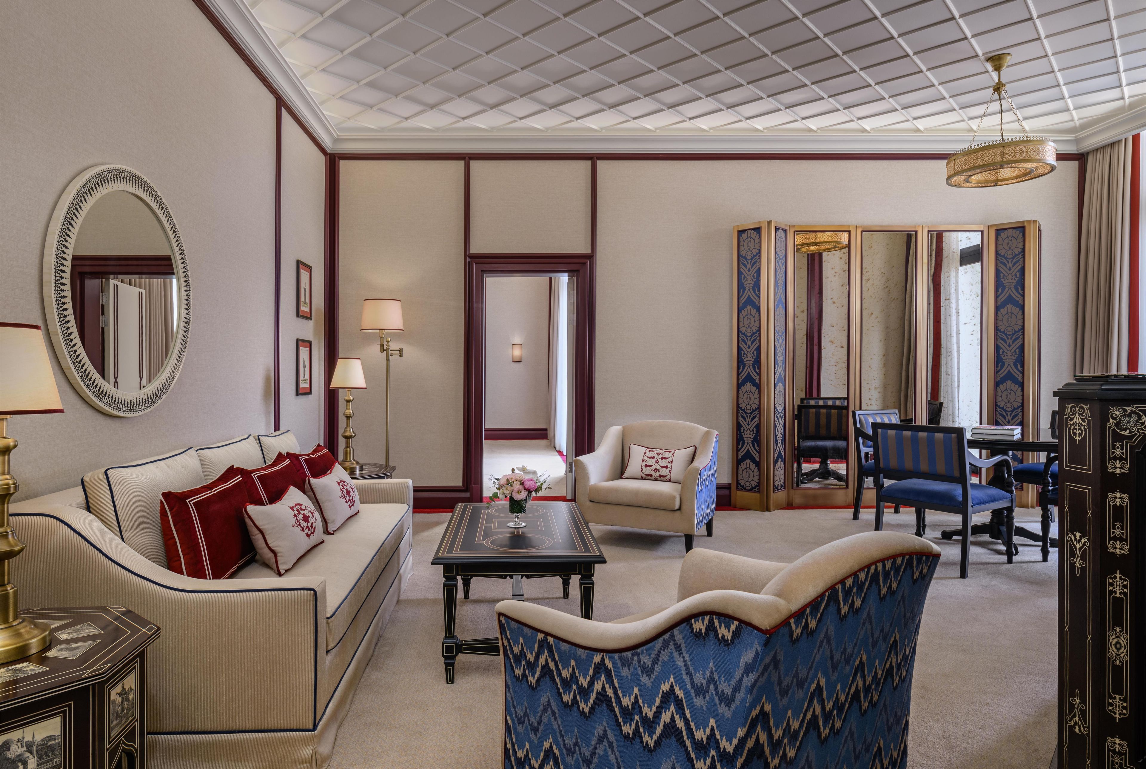 Une chambre d’hôtel équipée d’un canapé, de fauteuils, d’une table basse, d’un miroir et d’une lampe décorative.