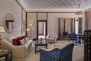 Una habitación de hotel con sofá, sillones, una mesa de centro, un espejo y una lámpara decorativa.