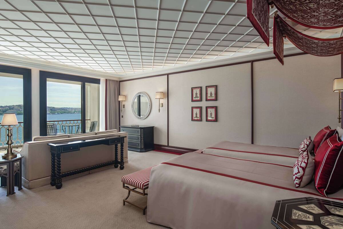 A hotel room with a large bed, a desk, a chair, a mirror, and a view of the city.