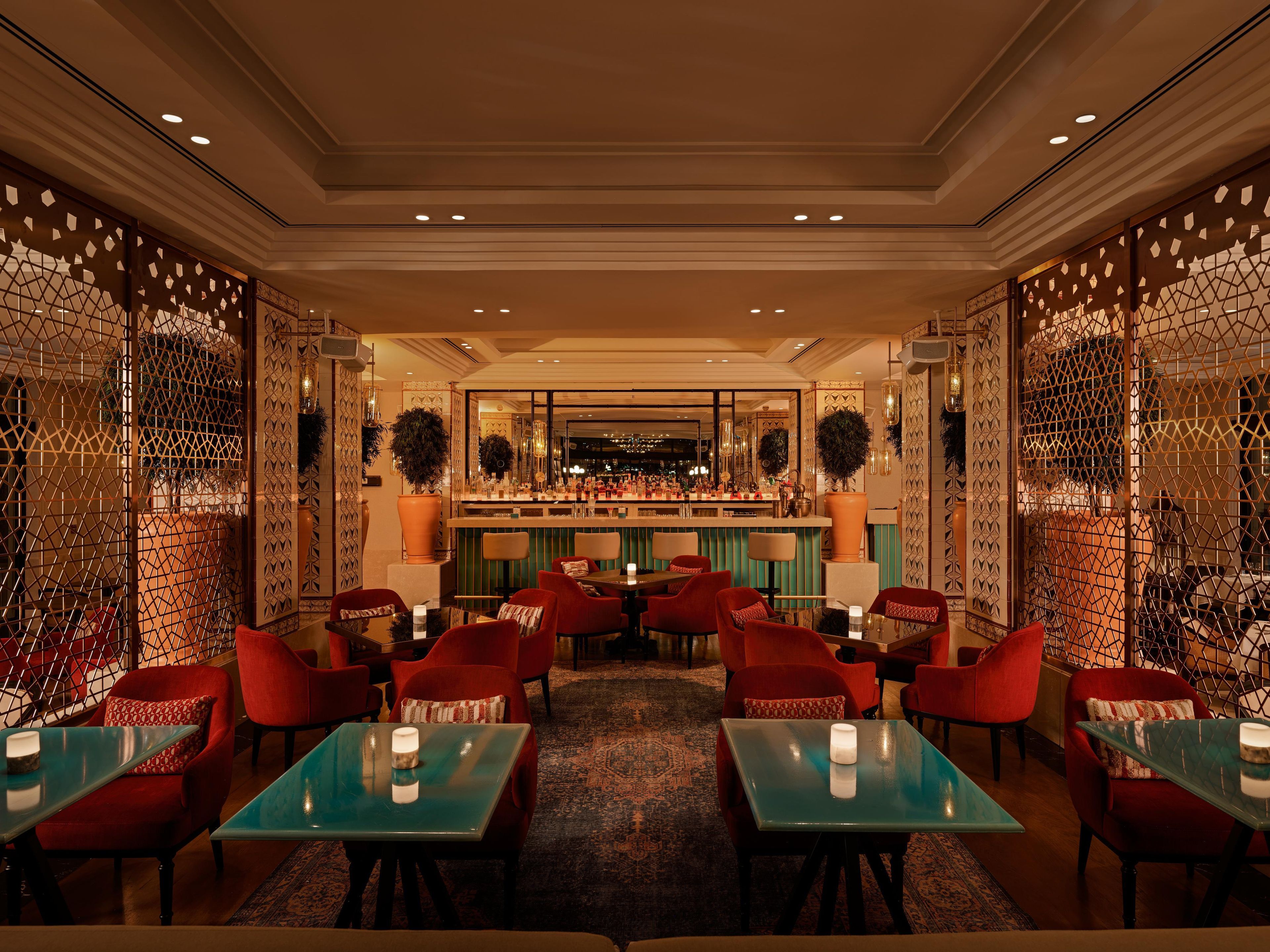 A bar area with multiple seating options, including red upholstered chairs and tables with glass tops.