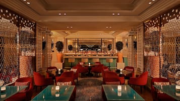 Un área de bar con varias opciones de asientos, incluyendo sillones tapizados en rojo y mesas con superficie de vidrio.