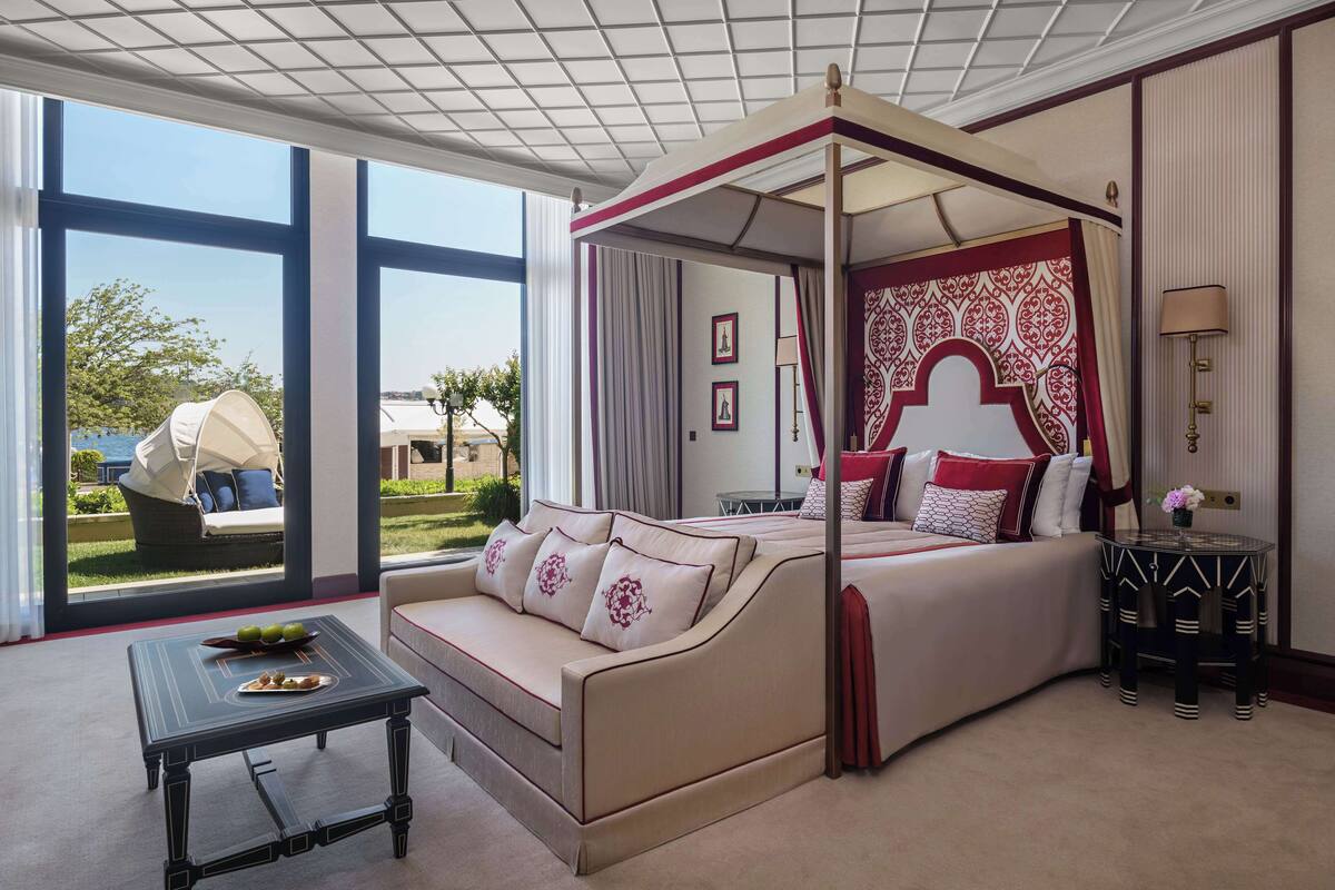 A four-poster bed with a canopy, a sofa, a small table, and a view of the outdoors.