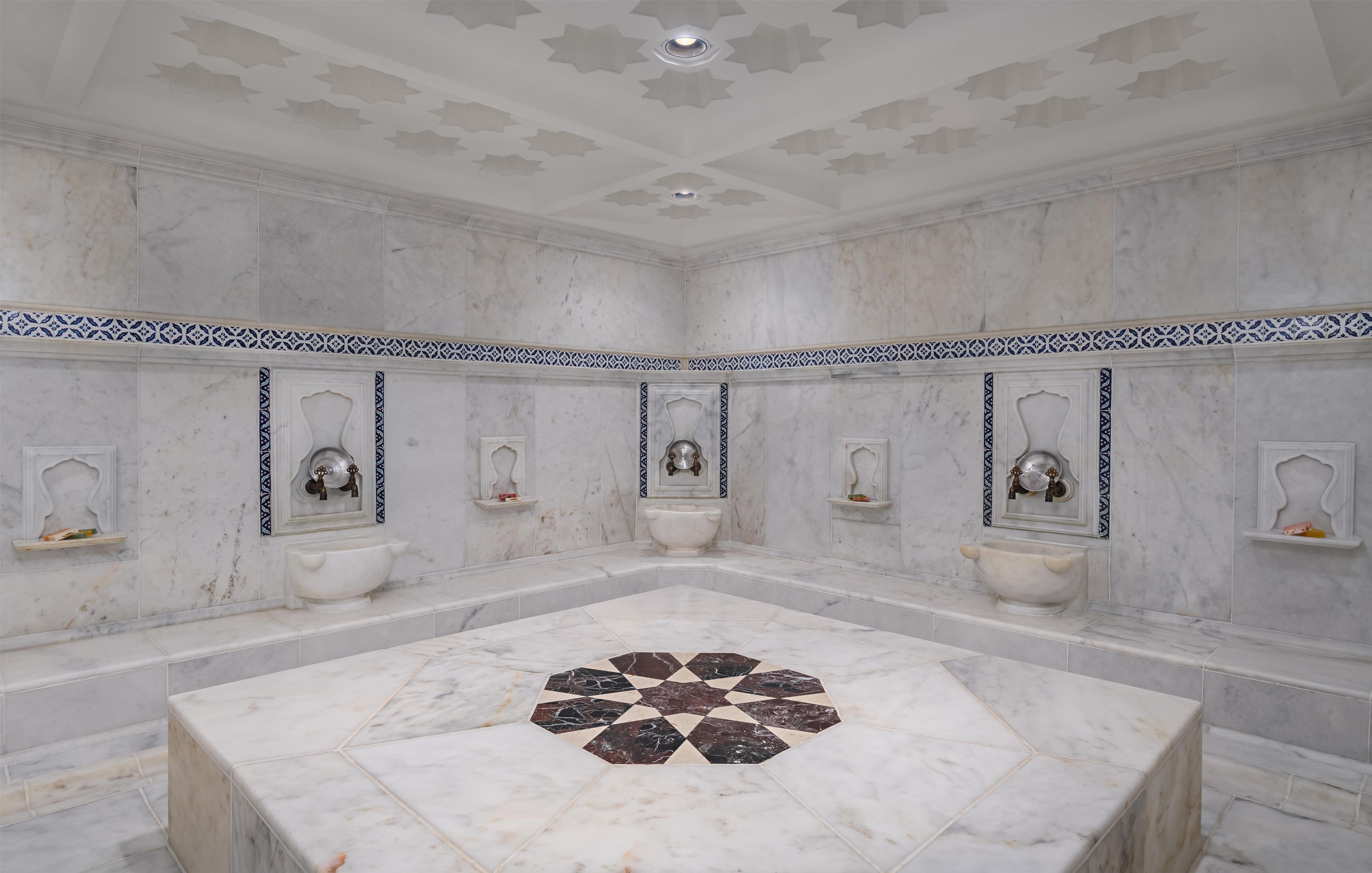 A large bathroom with a central marble sink, multiple smaller sinks, and a decorative floor pattern.
