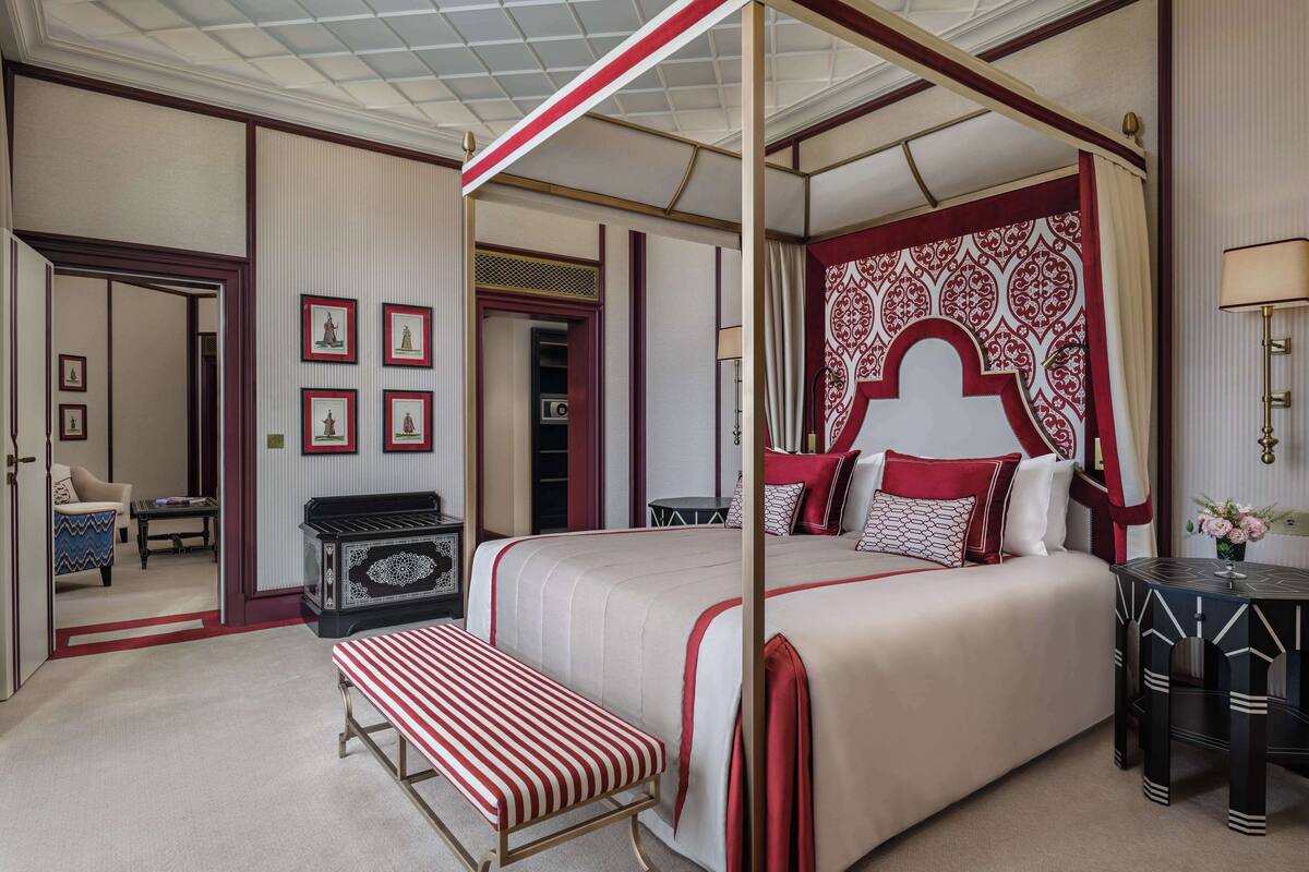 A four-poster bed with a red and white canopy, a bedside table, a bench, and a wall with framed pictures.
