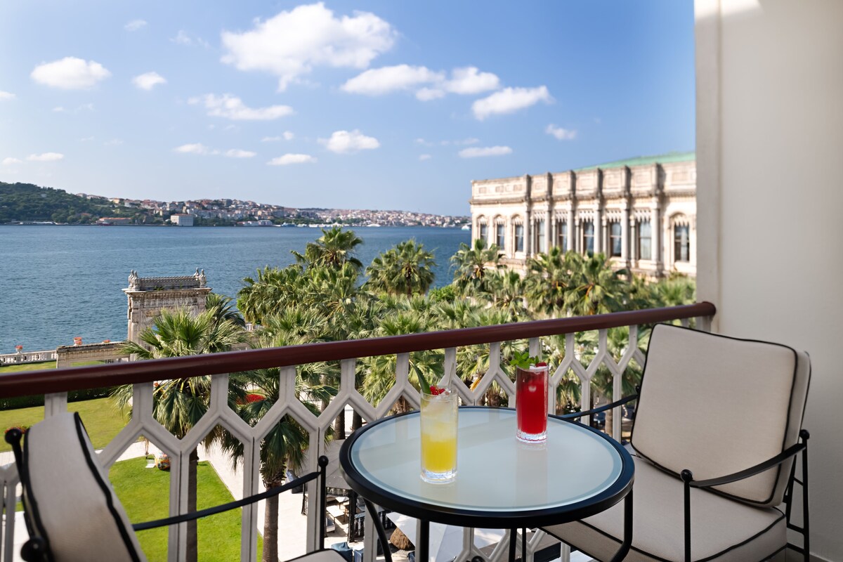 A balcony with a table and chairs, overlooking a body of water and a historic building.