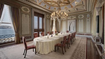 Een statige eetzaal met een grote ronde tafel, versierde stoelen en een kroonluchter.