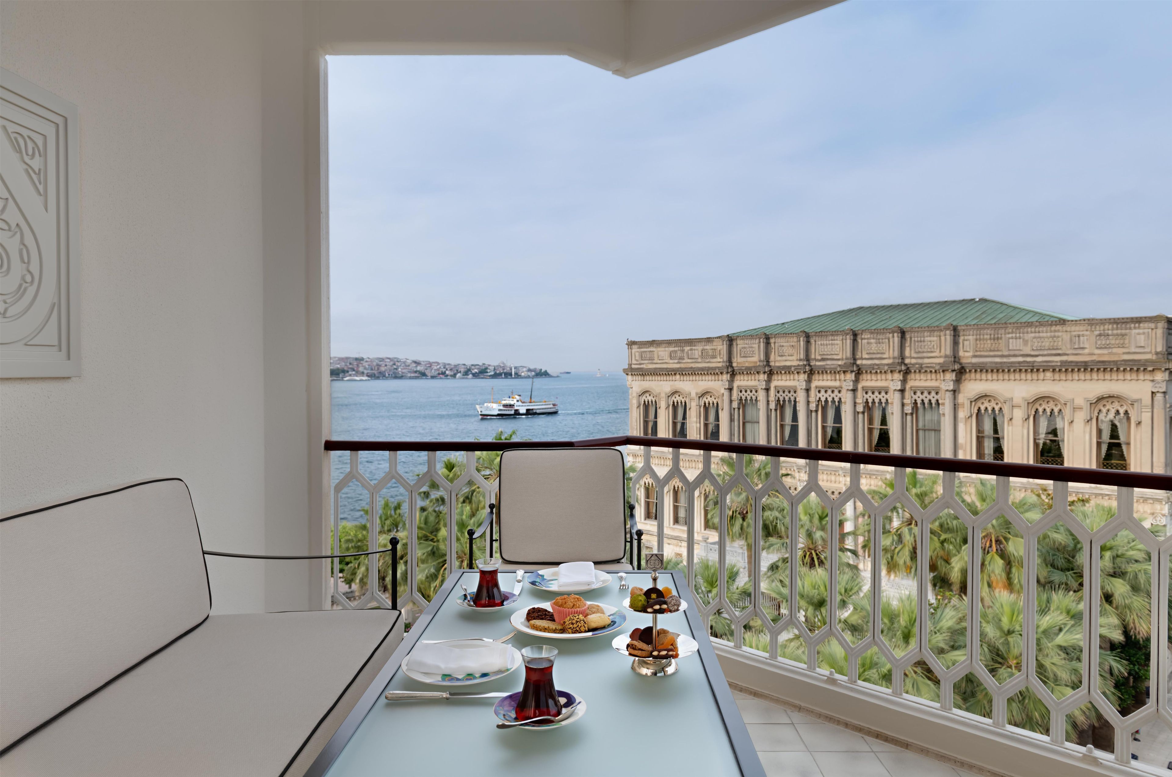 A balcony with a table set for a meal, overlooking a body of water and a historic building.