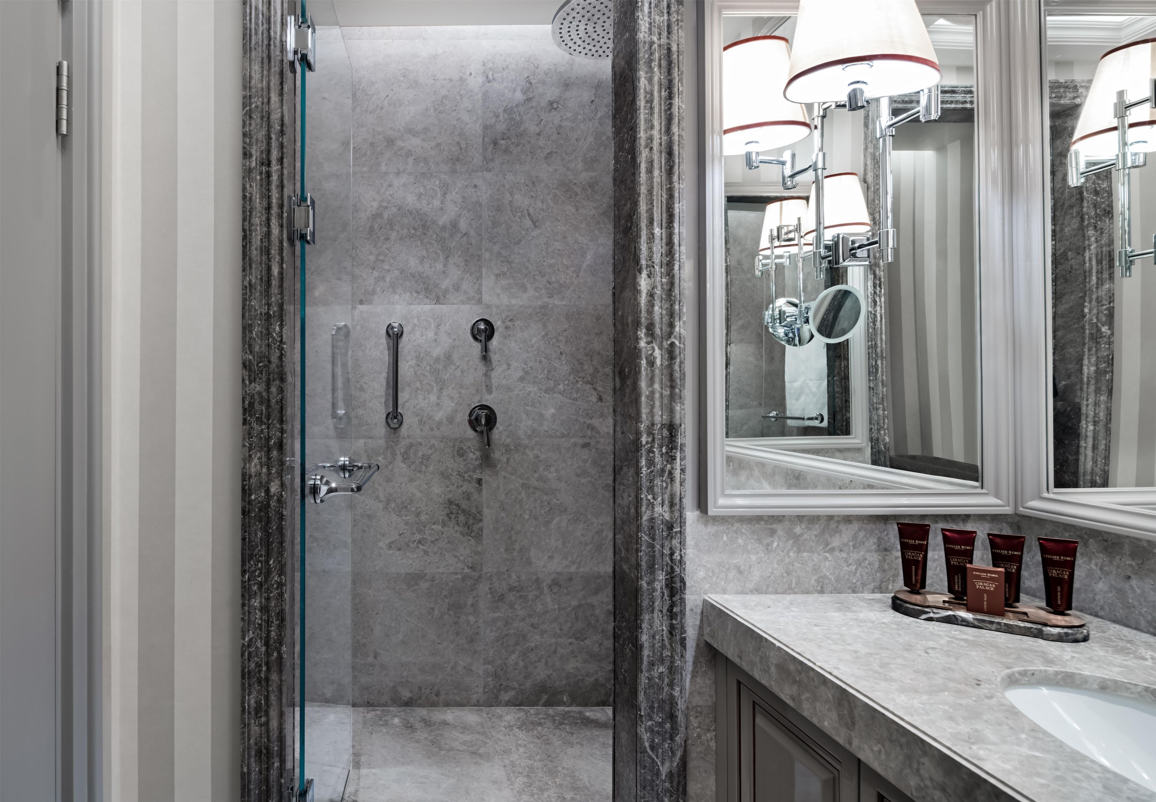 Un baño moderno con ducha de mármol, un espejo grande y un tocador con artículos de aseo.