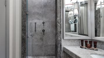 Un baño moderno con ducha de mármol, un espejo grande y un tocador con artículos de aseo.
