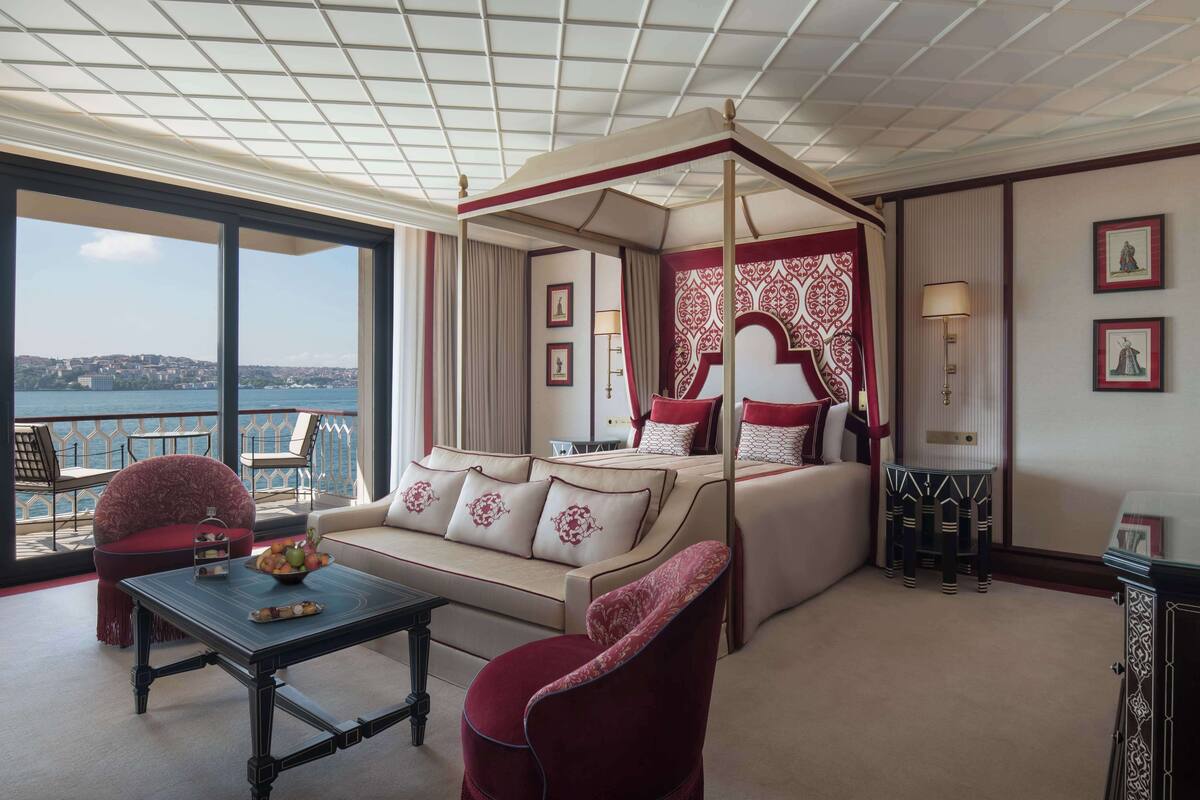 A spacious suite with a large bed, a sofa, a dining table, and a balcony with a view of the city and water.