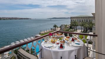 Una mesa servida con diversos platos y bebidas, con vista a un cuerpo de agua y un paisaje urbano al fondo.