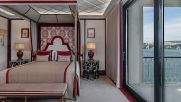 Una cama con dosel y cortinas, dos mesitas de noche con lámparas, un ventanal con vistas a un puente y al paisaje urbano, y una pared con diseño.