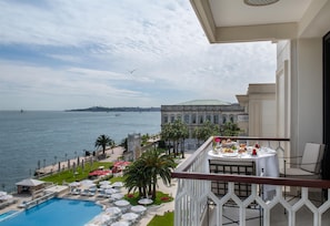 Un balcón con mesa lista para comer, con vista a una piscina y al mar.