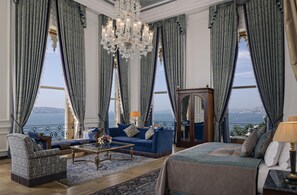 A spacious living room with a large chandelier, a sofa set, a coffee table, and a view of the sea. - Ciragan Palace Kempinski (Istanbul)
