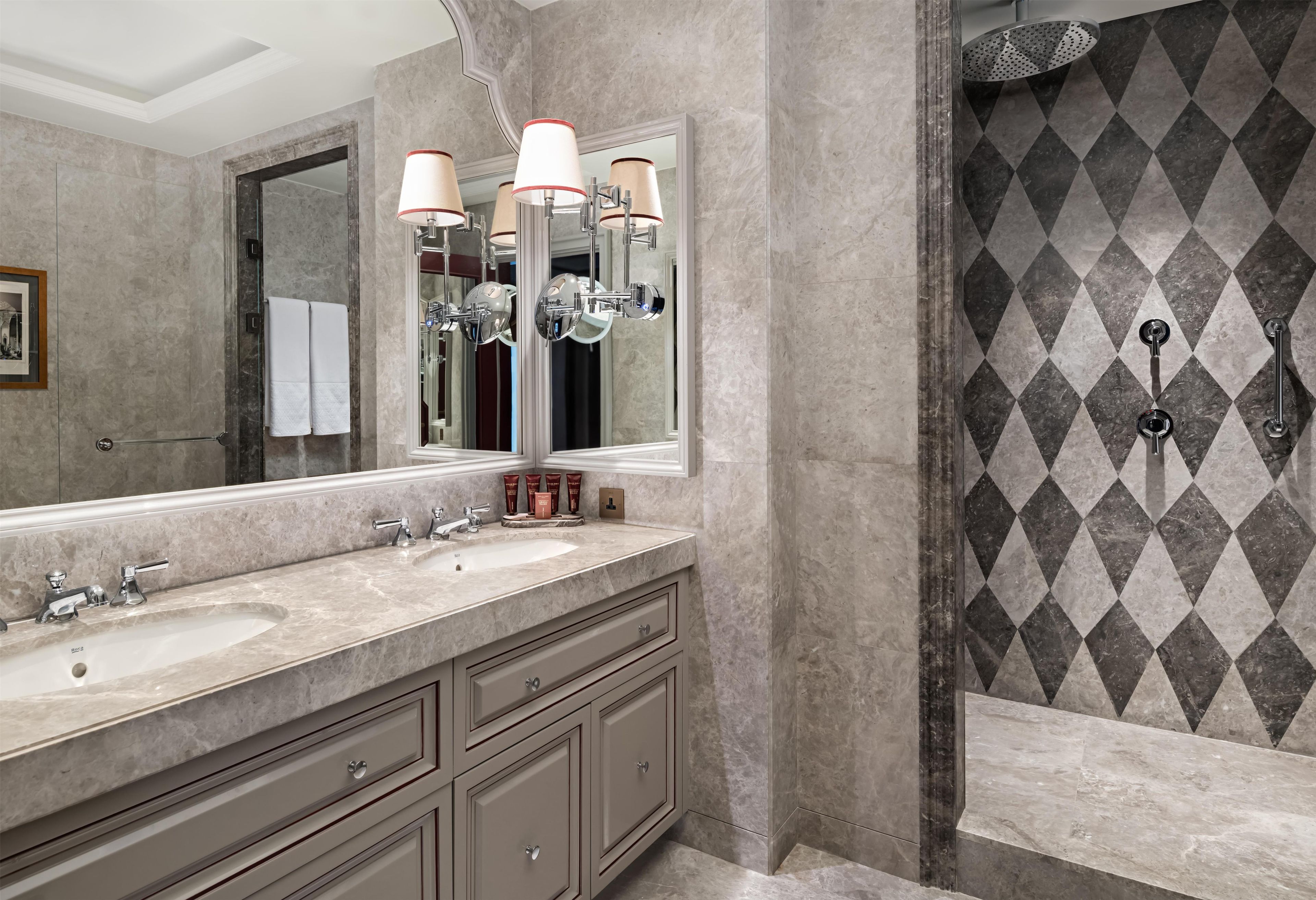 A bathroom with two sinks, a large mirror, and a shower with a diamond-patterned wall.