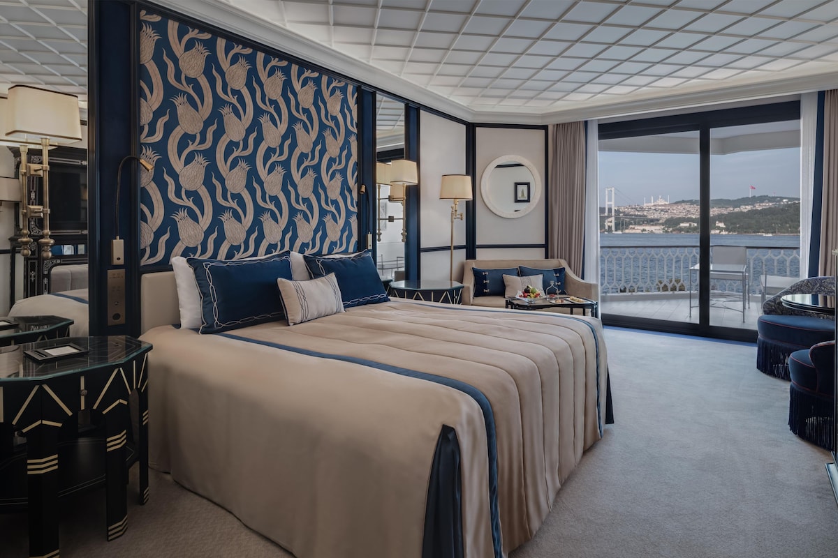 Habitación de hotel con una cama grande, un balcón y vistas a un puente y al paisaje urbano.