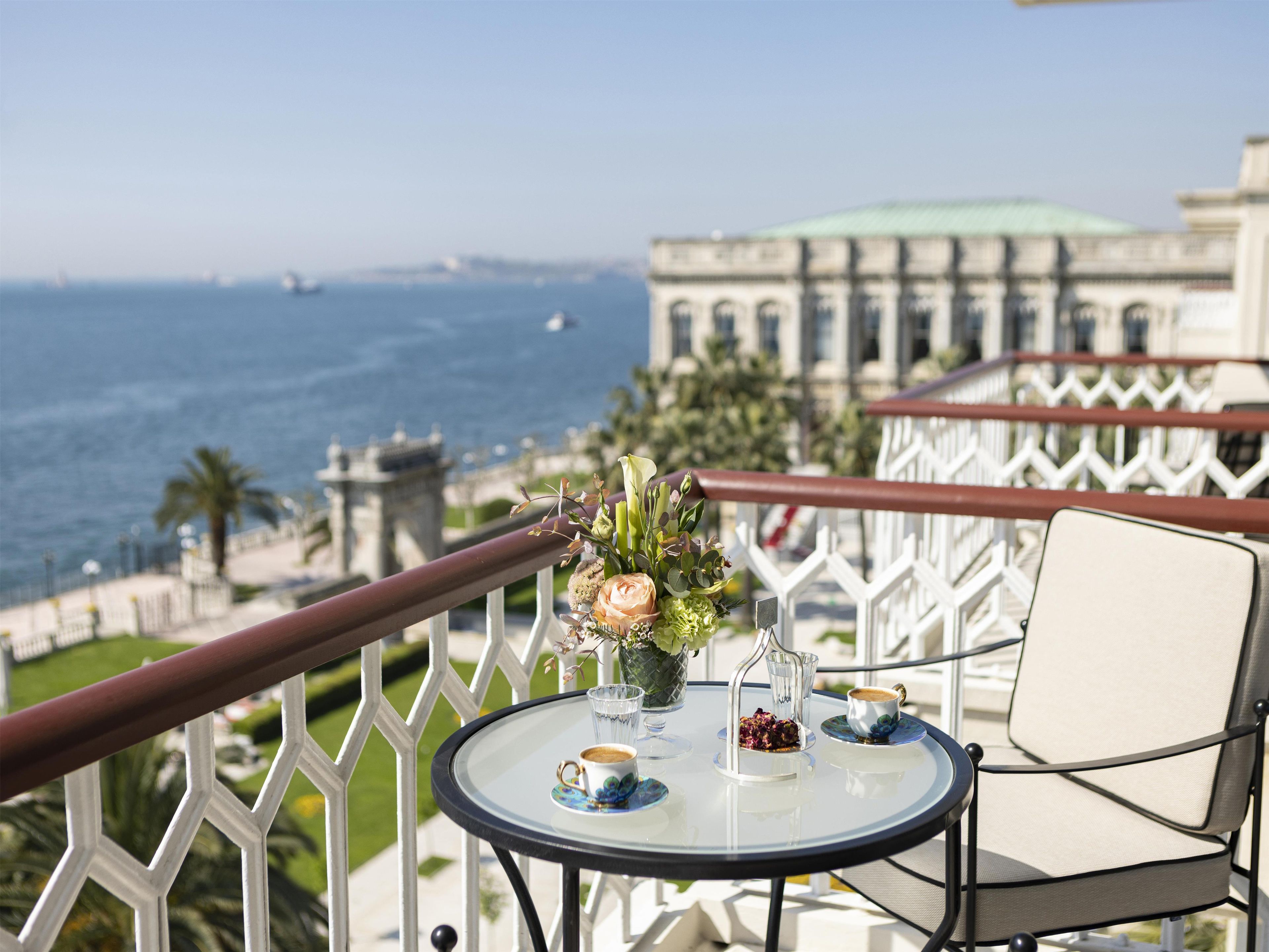 Un balcón con una mesa lista para dos personas, con vista a un cuerpo de agua y un edificio histórico.