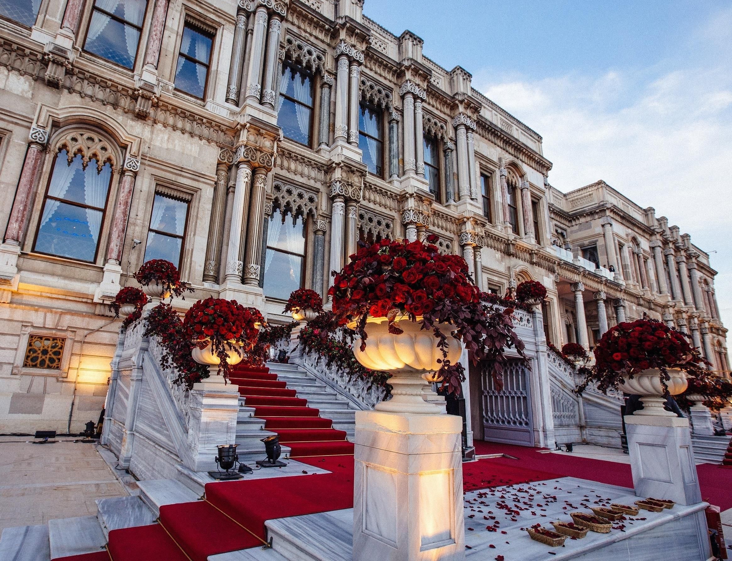 A grand building with ornate architecture, a staircase with red carpet, and large flower arrangements.