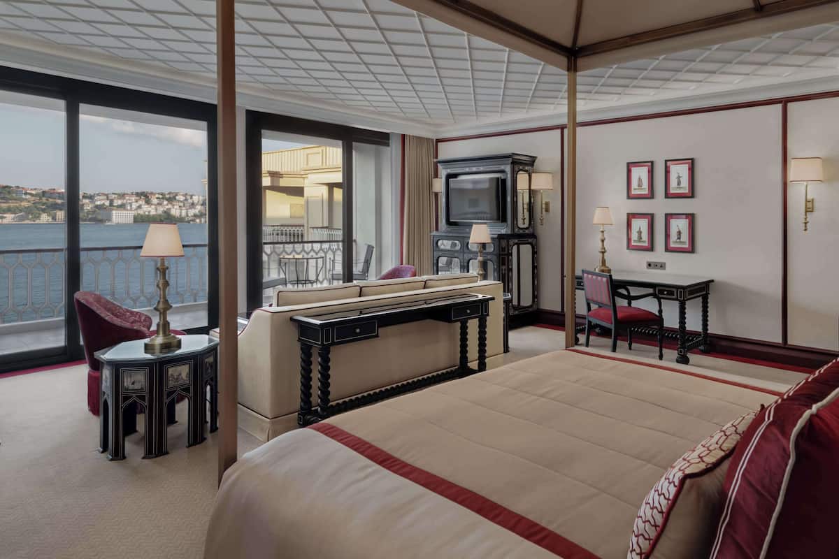 A hotel room with a large bed, a desk, a television, and a view of the city.